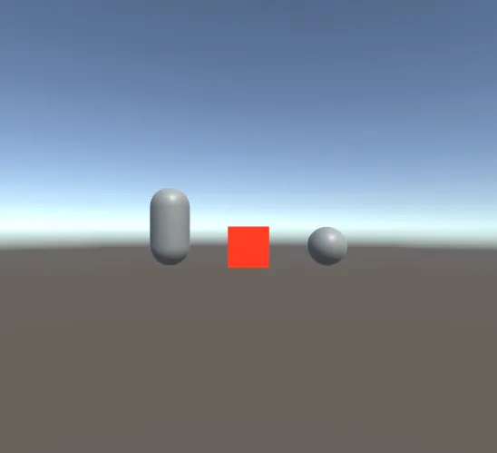 The same capsule, cube and sphere on the same ground and sky, but the cube is now bright red.