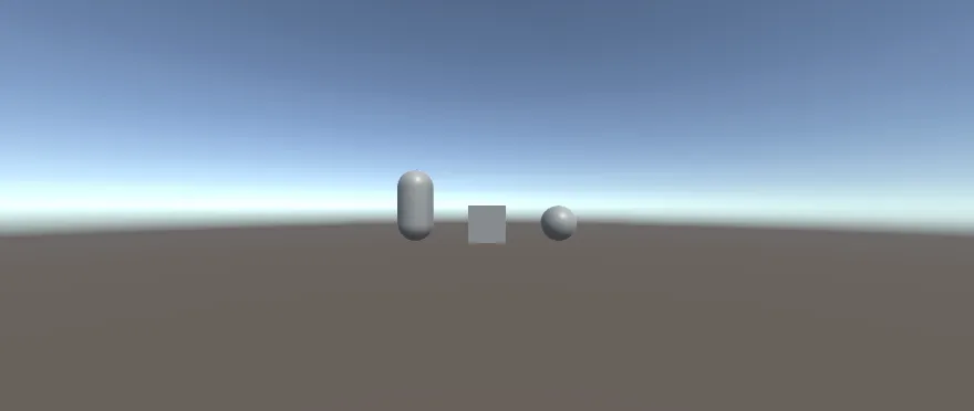 A grey capsule, a grey cube and a grey sphere stand in a row on flat brown ground under a sky that fades from blue to white at the horizon.